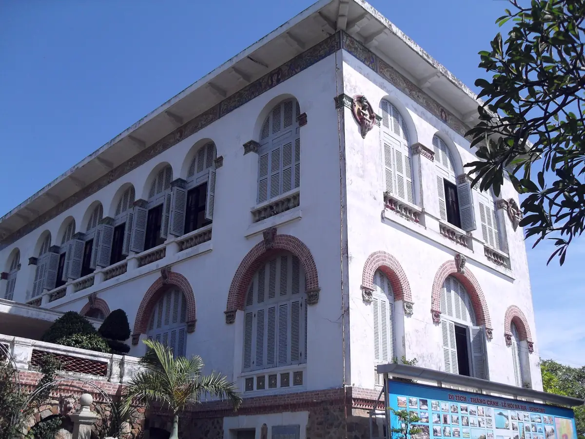 Colonial white villa facade with arched windows and tropical trees