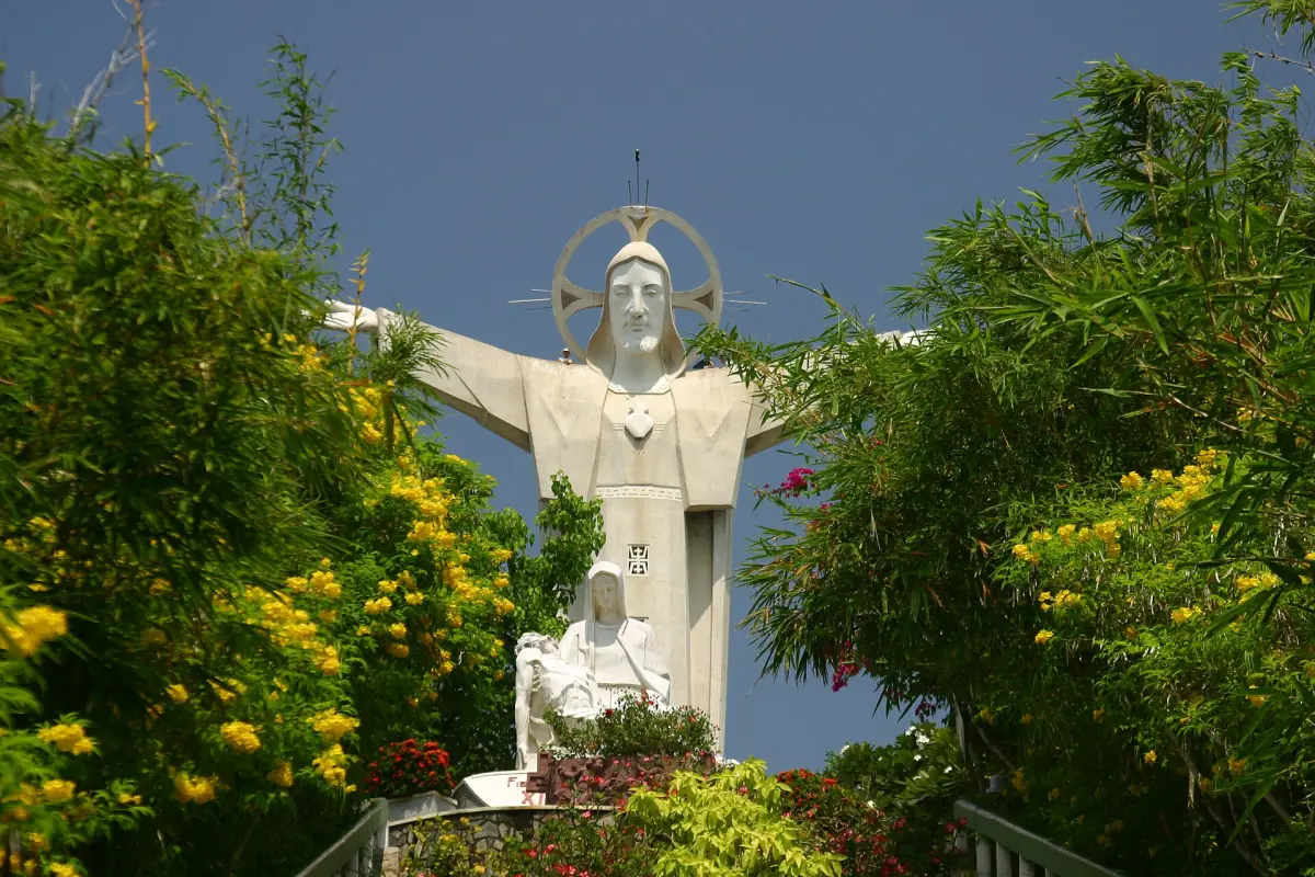 Christ statue with raised arm beside yellow flowering trees and dark sky