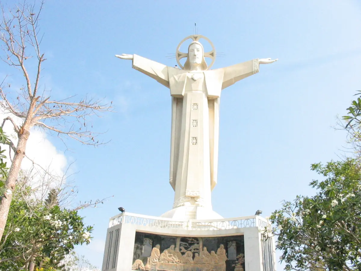 White Christ statue with outstretched arms against a pale blue sky