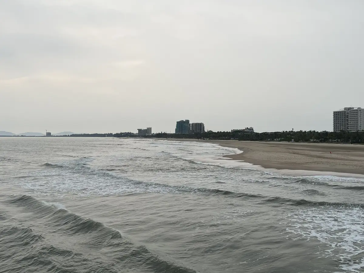 Grey overcast sky over waves rolling onto a long Ho Tram beach