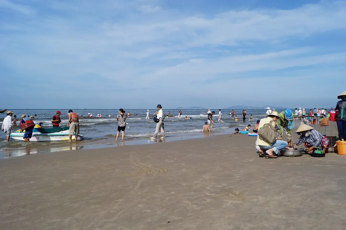 Long Hai beach with fishing boats, bathers and a hazy blue sky